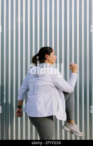 Side view of plus size active young ethnic female athlete in sportswear doing steps exercise while working out on city street in sunny morning Stock Photo