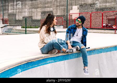 Full body of happy young man and Woman speaking while resting on gray parapet Stock Photo