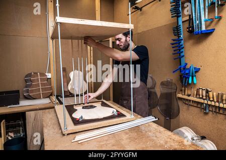 Side view of adult male luthier inserting sticks into wooden planks with musical instrument sound board in workshop Stock Photo