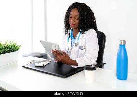 African American female doctor with stethoscope scrolling tablet while working in clinic Stock Photo