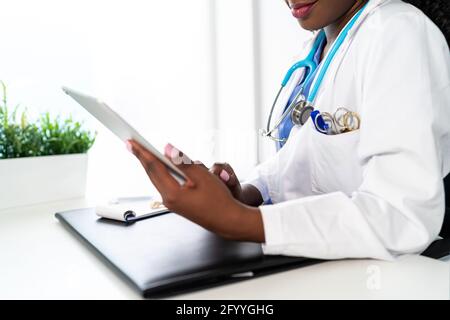 Cropped unrecognizable African American female doctor with stethoscope scrolling tablet while working in clinic Stock Photo