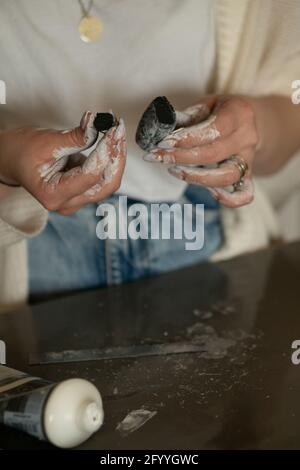 Crop anonymous female jewelry designer with dirty hands cutting clay while working in craftsmanship Stock Photo