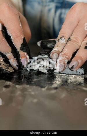 Crop anonymous female jewelry designer with dirty hands cutting clay while working in craftsmanship Stock Photo