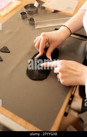 From above crop unrecognizable female jewelry maker forming details of black clay while working in light craftsmanship Stock Photo