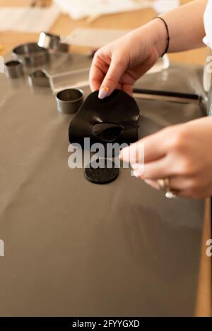 From above crop unrecognizable female jewelry maker forming details of black clay while working in light craftsmanship Stock Photo