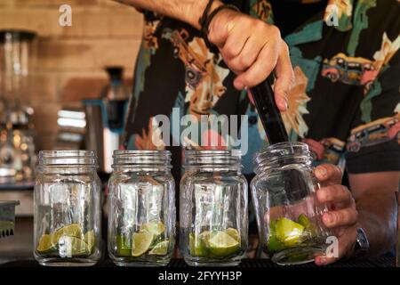 Crop anonymous male bartender squeezing ripe limes in jars while preparing mojito in bar Stock Photo