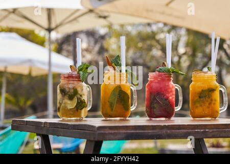 Set of refreshing various mojito cocktails including strawberry peach and classic flavors served on table in lush garden Stock Photo