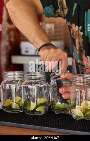 Crop anonymous male bartender squeezing ripe limes in jars while preparing mojito in bar Stock Photo