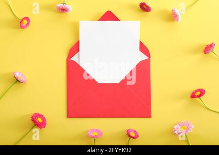 Red open envelope with blank paper card mockup and wildflowers on yellow background. Flat lay composition, top view, copy space. Love letter, romance Stock Photo
