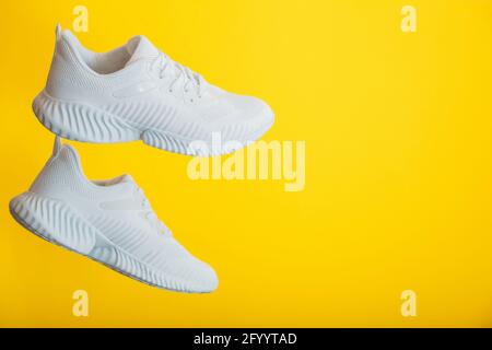 White sneakers shoes fly on yellow background. Pair of Modern jogging sports male white sneakers on color wall with copy space. Stock Photo