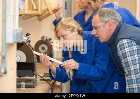 supervisor watching female apprentice carpenter use grinding wheel Stock Photo
