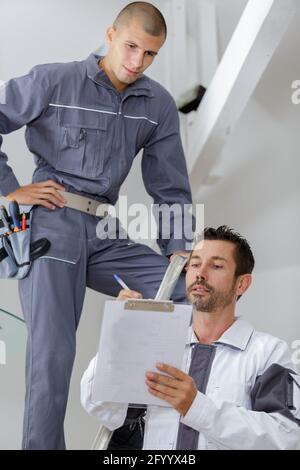 foreman giving instructions to apprentice on stepladder Stock Photo