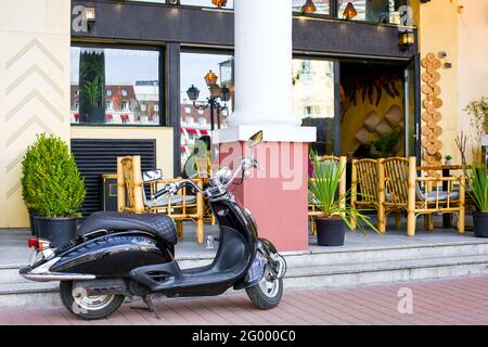 black moped motorcycle vehicle in front of the street cafe building with bamboo chairs in chinese style and pots with plants, empty nobody. Stock Photo