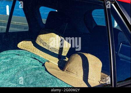 Two straw sun hats rest on a green towel in the back of a car - Summertime Stock Photo