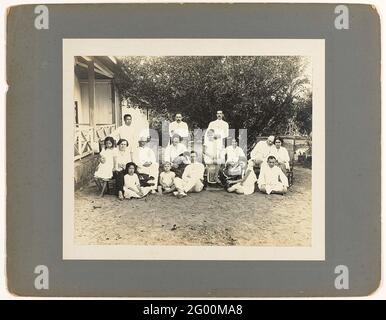 Portrait of family boers with staff. Group photo of the Robert Julius Boers family, Chef of the banka tin recovery, with staff, total 16 people. Left part of the porch of the wooden house; In background bushes. Stuck on dark gray cardboard. Stock Photo