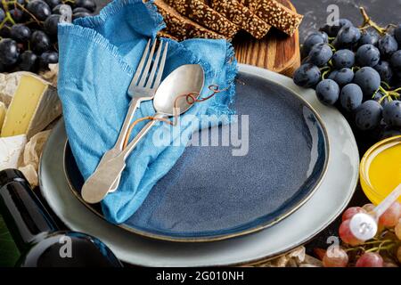 Empty serving blue plate with fork spoon in frame of food ingredients Mediterranean Kitchen gastronomy appetizer snacks grapes cheese wine. Mock up Stock Photo