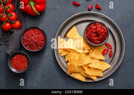 Composition with tasty chili sauce, ingredients and nachos on dark background Stock Photo