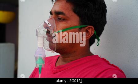 Young man is breathing with oxygen mask on face at the home during pandemic in India. Indian taking Emergency Oxygen with nebulizer mask outside Stock Photo