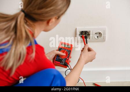 Young female electrician measuring voltage of socket at home Stock Photo