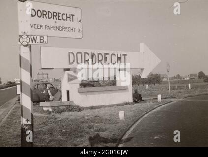 Anwb Plate: Dordrecht. Along a motorway is an ANWB board towards Dordrecht. In addition, a structure of stone with an arrow containing the inscription: Dordrecht. Below it a triangle with a flying bird. Reference to the Luftwaffe basis? A German soldier leans against the construction. There are two cars with a blond boy. Stock Photo