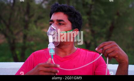 Young man inhale with oxygen mask on face during pandemic in India. A infected person with Covid 19 disease outside of hospital. Coronavirus Stock Photo