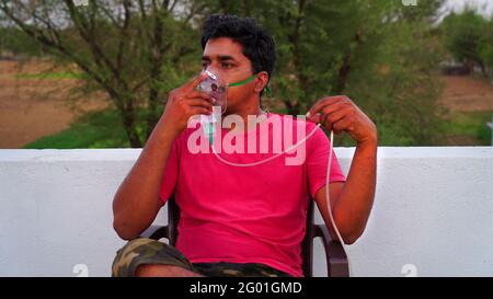 Young man inhale with oxygen mask on face during pandemic in India. A infected person with Covid 19 disease outside of hospital. Coronavirus Stock Photo
