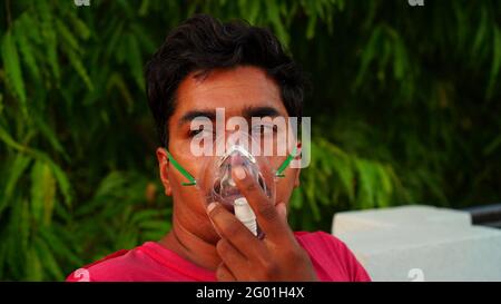 Young man is breathing with oxygen mask on face at the home during pandemic in India. Indian taking Emergency Oxygen with nebulizer mask outside Stock Photo