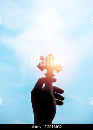 Jigsaw puzzle against blue sky background with copy space, silhouette, vertical style. Hand of businessman holding puzzle with sunlight. Business solu Stock Photo