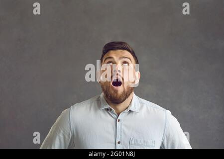 Shocked man with opened mouth widely looking overhead closeup portrait