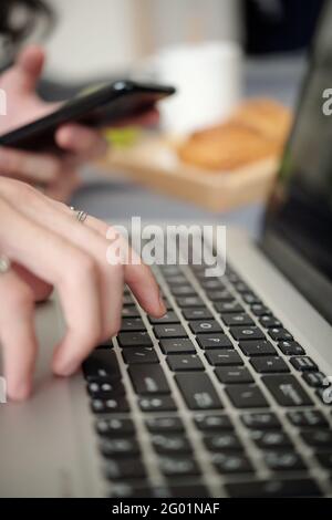 Close-up of unrecognizable man using smartphone while typing on laptop keyboard, inserting verification code Stock Photo