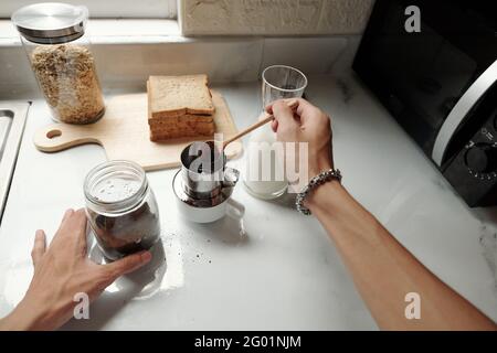 Close-up of unrecognizable man with bracelet putting ground coffee into brewer while making coffee in kitchen Stock Photo