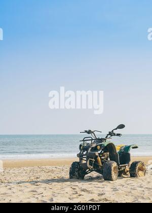 Vintage green ATV on the sandy beach. Quad ATV all terrain vehicle parked on beach, Motor bikes ready for action with summer sun flaring on bright day Stock Photo