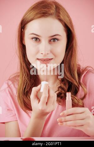 Portrait of young beautiful red haired woman applying pink matte liquid lipstick Stock Photo
