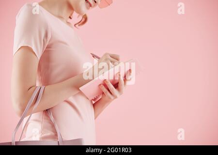 Cropped image of smiling young businesswoman in pink dress writing her thoughts and ideas in planner Stock Photo