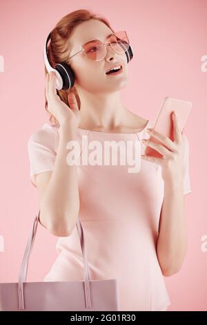 Portrait of beautiful pretty young woman in pink sunglasses enjoying listening to music on her phone Stock Photo