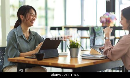 Side view of two female workers smiling and talking to each other while meeting on their project Stock Photo