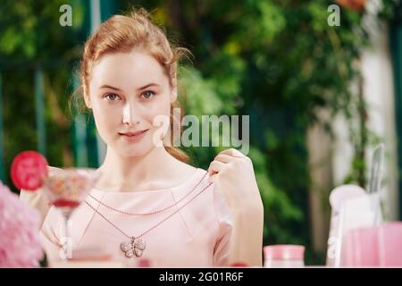 Portrait of pretty smiling young woman trying on beautiful necklace at outdoor party Stock Photo