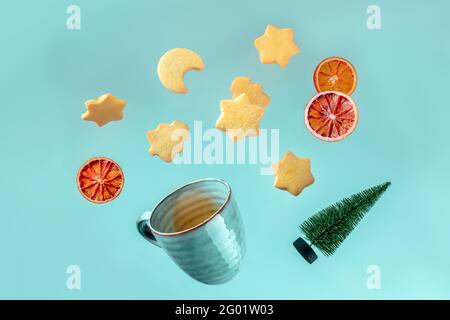 Christmas greeting card with falling cookies, a cup of tea, and a Christmas tree on a light blue background, with dried oranges Stock Photo