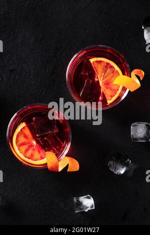 Negroni cocktails with orange rind, shot from the top with ice cubes on a black background, with copy space