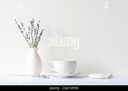Still life with minimal composition, lavender dried bouquet, ceramic white cup and hot beverage tea or coffee, morning mood in beige tone Stock Photo