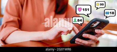Hands of young woman using smartphone in cafe. Bubbles of social media and connections icons popping out of mobile phone - Panoramic banner size with copy space Stock Photo