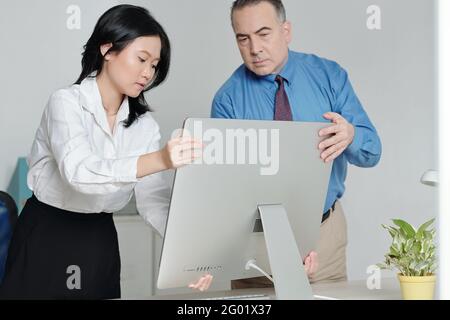 Mature serious man helping new colleague to put computer at her office desk Stock Photo