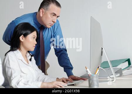 Serious entrepreneur looking at computer screen of employee working on important task Stock Photo