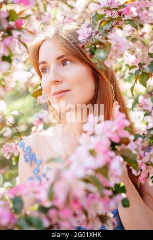 Portrait of a red-haired girl against a background of pink flowers. Stock Photo