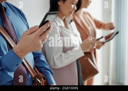 Hands of mature man checking his phone when standing in queue to job interview in office, selective focus Stock Photo