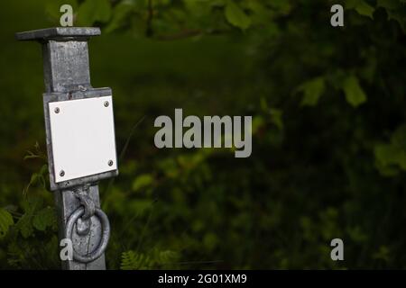metal post with blank white sign in front of blurry green natural background Stock Photo