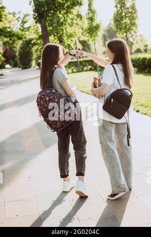Two female students greet each other with their fists when they meet on campus. Distance learning. Soft selective focus. Stock Photo