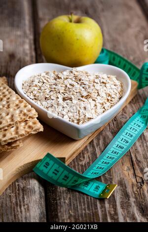 Oatmeal in a heart-shaped plate, green apple and measuring tape. Weight loss and diet concept. Stock Photo