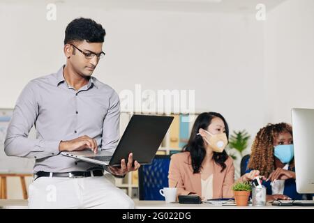 Confident intelligent software developer leaning on office table and working on laptop Stock Photo