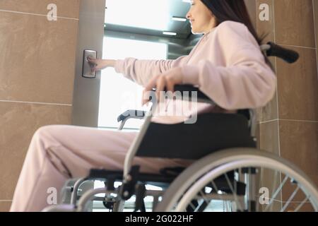 Smiling woman in wheelchair presses button of elevator Stock Photo